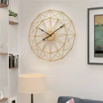 Relógio de parede com estrutura de linhas douradas formando um padrão geométrico, com ponteiros pretos e fundo dourado, em ambiente moderno com decoração minimalista.