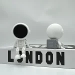 Figuras de astronauta e bola de golfe em miniatura, com detalhes de roupas espaciais e textura da bola, colocadas sobre uma base com a palavra 'LONDON'.