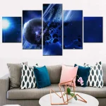 Conjunto de cinco quadros com imagem de espaço, planetas e estrelas em tons de azul e preto, decorando uma parede branca acima de um sofá cinzento com almofadas coloridas.