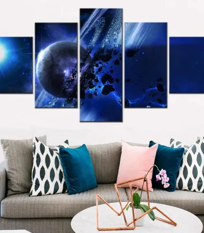Conjunto de cinco quadros com imagem de espaço, planetas e estrelas em tons de azul e preto, decorando uma parede branca acima de um sofá cinzento com almofadas coloridas.