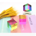 Três cubos de plástico translúcido com cores vibrantes, vistos de diferentes ângulos, com um pacote de trigo e papel colorido ao fundo.