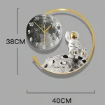 Relógio de parede com esfera lunar, astronauta em superfície lunar e arco dourado, medindo 38cm de altura e 40cm de largura.
