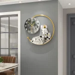 Relógio de parede com design de lua e astronauta em uma parede cinzenta, com detalhes dourados e uma esfera lunar decorativa.