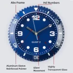 Relógio de parede com moldura de vidro transparente, mostrador azul com números grandes e ponteiros de cores diferentes, detalhes de acabamento em alumínio e movimento silencioso.