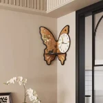Relógio de parede com design de borboleta, com detalhes em madeira e um mostrador analógico, decorando uma parede branca moderna.