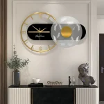 Relógio de parede com moldura dourada, fundo preto e detalhes em branco e dourado, decorando uma parede branca com elementos decorativos ao lado.