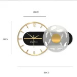 Relógio de parede com moldura dourada, fundo preto e detalhes em branco, medindo 36cm de diâmetro, com um disco de vidro decorativo ao lado.