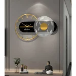 Relógio de parede com moldura dourada, fundo preto e detalhes em branco, decorando uma parede cinzenta com uma esfera decorativa ao lado.