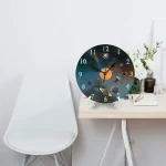 Relógio de parede com design de espaço, planetas e estrelas, colocado numa mesa junto a uma cadeira branca e uma planta com flores brancas.