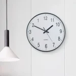 Relógio de parede com mostrador branco, números grandes e ponteiros pretos, exibindo a hora 10:09.