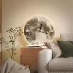 Relógio de parede com fundo de textura metálica, iluminação indireta, ao lado de uma mesa de cabeceira com livros e uma planta decorativa.
