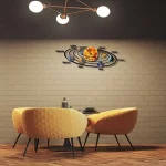 Sistema solar decorativo na parede com nomes dos planetas e o Sol, iluminado por luzes de teto, acima de uma mesa de jantar com cadeiras amarelas.