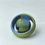 Bola de borracha verde com textura rugosa, contendo uma esfera de metal com acabamento colorido dentro, vista de cima.