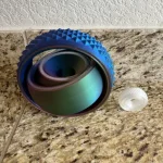 Lupa de aumento com estrutura azul com textura em relevo e luz LED integrada, colocada numa superfície de pedra, com botão de liga/desliga ao lado.