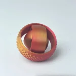 Anel de metal dourado com textura rugosa na parte exterior e interior lisa, colocado sobre fundo branco.