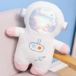 Pelúcia de astronauta com espelho holográfico na cabeça, braços e pés em rosa e branco, em ambiente com parede azul e móvel de madeira.