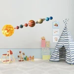 Modelo do sistema solar com planetas de diferentes tamanhos e cores, decorando uma parede branca de quarto infantil.