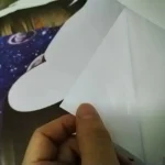 Mão a segurar papel branco a fazer origami, com fundo de tecido com tema espacial e estrelas.