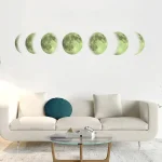 Fases da Lua em diferentes tamanhos e ângulos, decorando uma parede branca acima de um sofá branco com almofada azul escura.