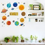 Decoração de parede com planetas, estrelas, sol e outros corpos celestes em cores vivas, acompanhada por prateleiras com plantas e objetos decorativos.
