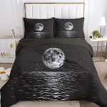Conjunto de roupa de cama preto com ilustrações de lua cheia e estrelas, incluindo duas almofadas com imagens de lua no topo da cama.