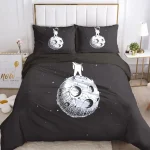 Conjunto de roupa de cama preto com ilustrações de lua e astronauta em estilo desenhado a branco, incluindo duas almofadas com imagens de lua em diferentes ângulos.