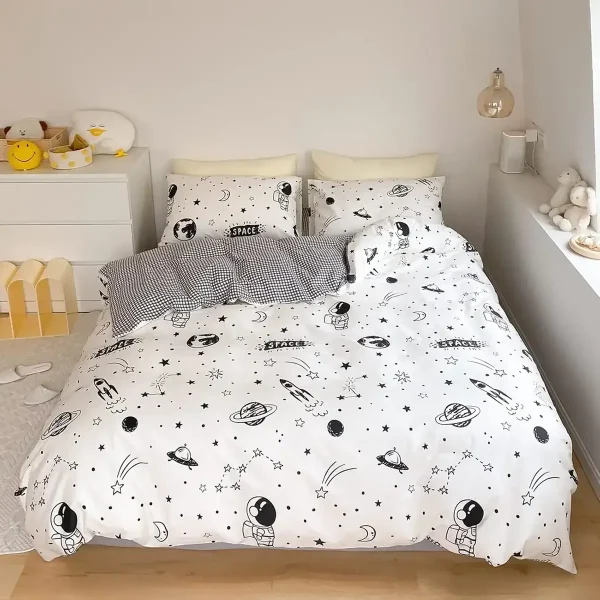 Roupa de cama com padrão de planetas, estrelas e astronautas, incluindo duas almofadas com desenhos de espaço, numa decoração de quarto infantil com tema espacial.