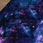 Duas almofadas com padrão de galáxia, estrelas e nebulosas em tons de azul, roxo e preto, colocadas sobre uma superfície escura.