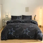 Conjunto de roupa de cama preto com estrelas azuis e detalhes de galáxias, incluindo duas almofadas e edredon, numa decoração moderna de quarto.