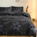 Conjunto de roupa de cama preto com estrelas azuis e galáxias, vista de cima, com almofadas combinando, em quarto moderno com iluminação suave e lâmpada de pé ao lado.