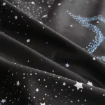 Tecido preto com padrão de estrelas brancas e azuis, detalhes de brilho e diferentes tamanhos de estrelas, ideal para projetos de decoração ou roupas temáticas.