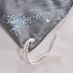 Detalhe de um saco de decoração com estrelas, pontos luminosos e cordão de amarrar, em tecido cinza com padrão de estrelas e pontos brilhantes.