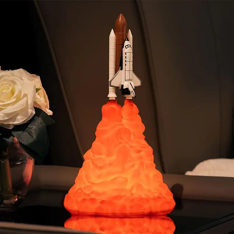 Foguete de brinquedo com detalhes de cores, lançado com efeito de fogo laranja, em fundo escuro, com flores brancas ao lado esquerdo.