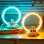 Luzes de anel LED azul e amarela com figuras de astronauta em base de rocha decorativa.