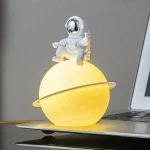 Miniatura de astronauta em traje espacial sentado numa esfera luminosa que representa um planeta com anel, sobre um portátil.