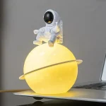 Miniatura de astronauta sentado numa esfera que representa um planeta, com iluminação amarela suave, sobre um portátil.