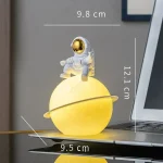 Miniatura de planeta amarelo com anel, astronauta em cima, junto a portátil, detalhes de dimensões.
