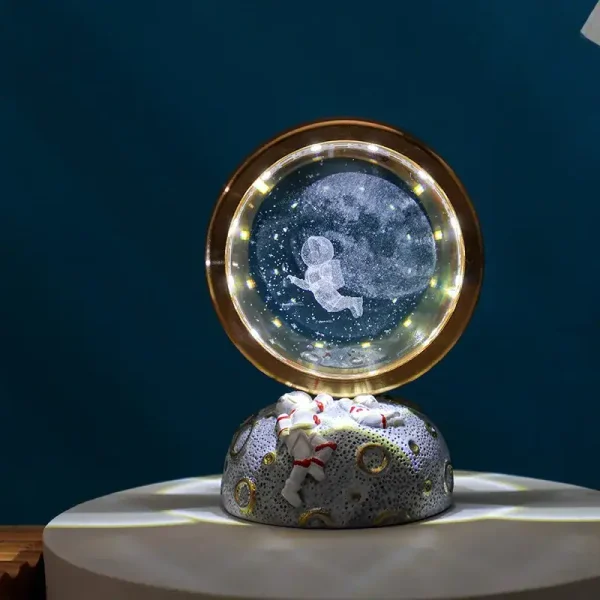 Globo de neve com figura de astronauta flutuando em espaço estrelado, base decorativa com padrão de planetas e estrelas, iluminação suave.