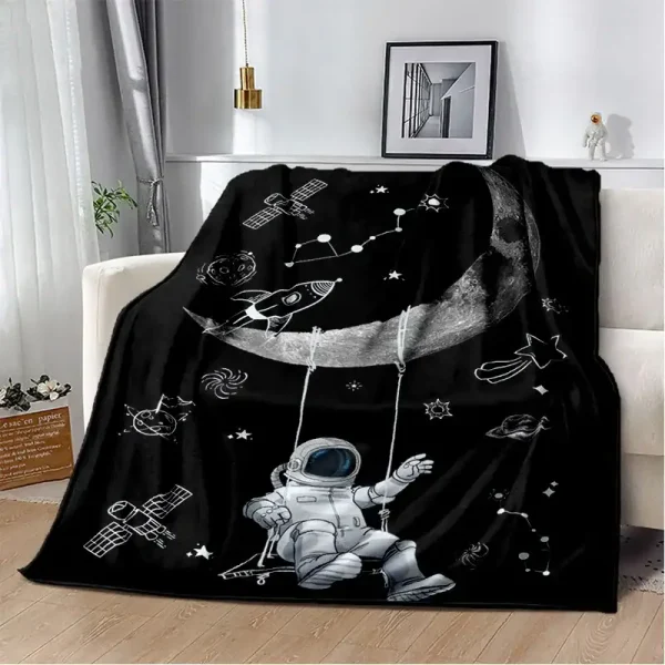 Manta preta com desenhos de astronauta, foguetes, estrelas e planetas, colocada sobre um sofá branco em sala de estar moderna.