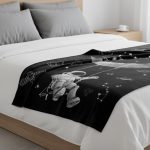 Manta preta com ilustração de astronauta e elementos espaciais, colocada sobre uma cama com roupa branca e almofadas cinzentas, em ambiente de quarto moderno.