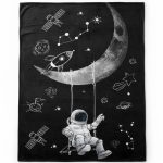 Manta preta com ilustração de astronauta a baloiçar na lua, estrelas, planetas e satélites em estilo desenhado a giz branco.