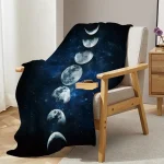 Manta de sofá com padrão de fases da Lua em tons de azul escuro e cinza, colocada sobre uma cadeira de madeira com almofada branca, ao lado de uma mesa de cabeceira com uma planta roxa.