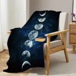Manta de tecido com ilustração das fases da Lua, colocada sobre uma cadeira de descanso de madeira e tecido claro, numa sala com cortinas brancas e móvel de madeira ao lado.