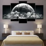 Quadro decorativo de várias painéis com imagem da lua cheia e nuvens, colocado acima da cama em quarto moderno com iluminação suave.