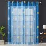 Cortinas azuis com estrelas, planetas e luas, decorando uma janela de quarto infantil com parede cinza escuro e plantas verdes ao lado.