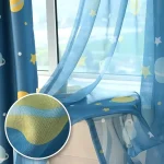 Cortina de tecido azul com estrelas, planetas e luas, decorando uma janela com vista para o exterior.