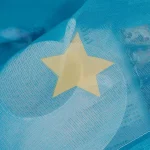Estrela de papel amarela colada na superfície de um balão de festa azul translúcido, com detalhes de textura e transparência.