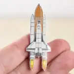Pin's en forme de vaisseau spatial avec détails en métal, illustrant une fusée prête à décoller, parfait pour les amateurs d'astronomie et de science.