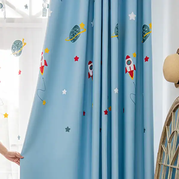 Cortina azul com desenhos de foguetes, planetas e estrelas, decorando um quarto infantil com tema espacial.