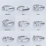 Conjunto de sete anéis de prata, cada um representando um signo zodiacal com detalhes brilhantes e design delicado.